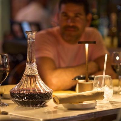 Crystal decanter of red wine on table, a person seated behind it.