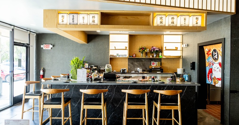 A black marble counter, wooden bar stools, illuminated Japanese signs, colorful wall artwork