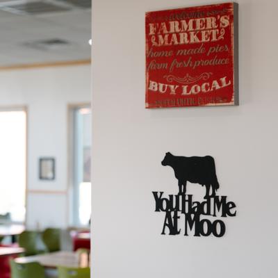 Interior, a wall with Farmer's Market sign and black cow silhouette reading You Had Me At Moo.