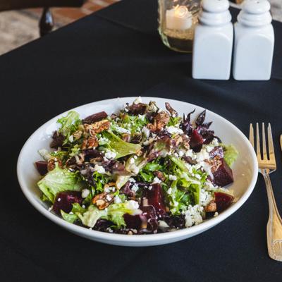 Roasted Beet & Goat Cheese Salad bowl served on a dark tablecloth.