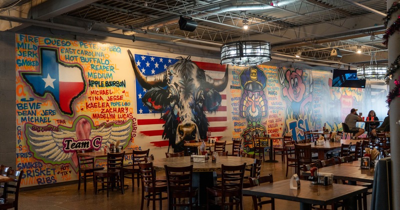 Colorful restaurant interior with wooden tables and chairs and a large murals on the wall