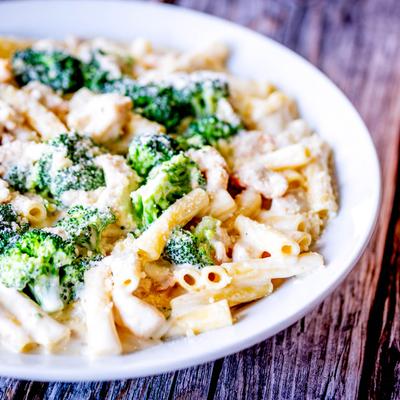 A plate of chicken broccoli ziti on a wooden table.