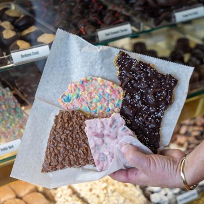A hand holds a sheet of parchment paper filled with varieties of chocolate bark.