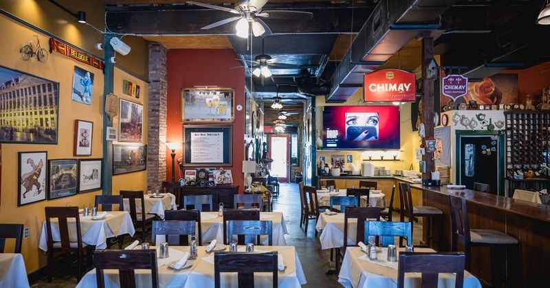 Interior of a restaurant with white tablecloths, wooden chairs, framed art