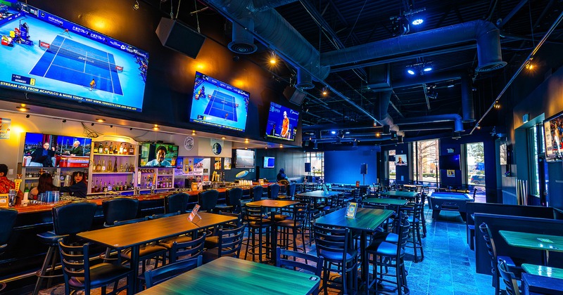 Spacious and cozy sports bar seating area and bar area with TV sets above the bar counter