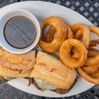 French Dip sandwich served with au jus and a side of onion rings.