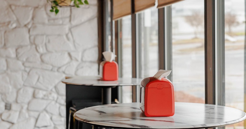 Interior, a row of marble topped tables with tissue dispensers, stools, and hanging plants above