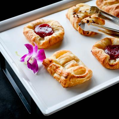 Assorted pastries on a plate with tongs and a purple orchid decoration.
