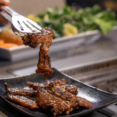 Grilled marinated beef short ribs being lifted from a plate, close-up.