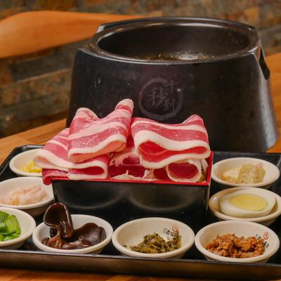 Sliced marbled beef arranged on a tray with a hot pot setup with other ingredients.