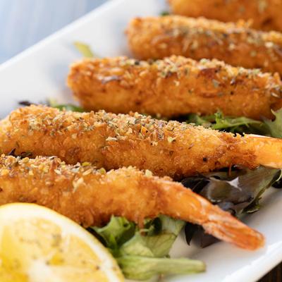 Shrimp Tempura served over a bed of greens with lemon slices on the side, close up.