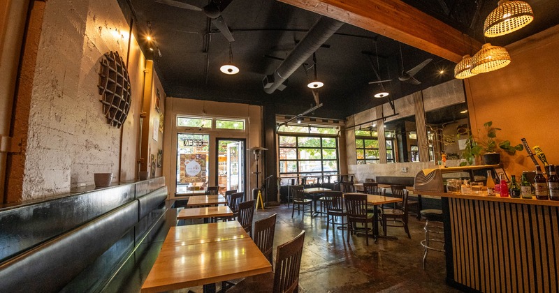 Cozy interior with wooden tables, dark chairs and a bar area under a warm-lit ceiling