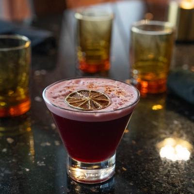 Dark red cocktail in a stemless martini glass with lime garnish.