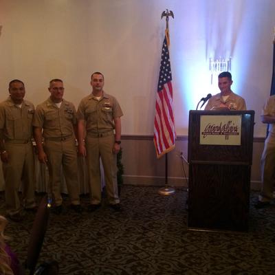 Four navy officers standing near a podium with an American flag.