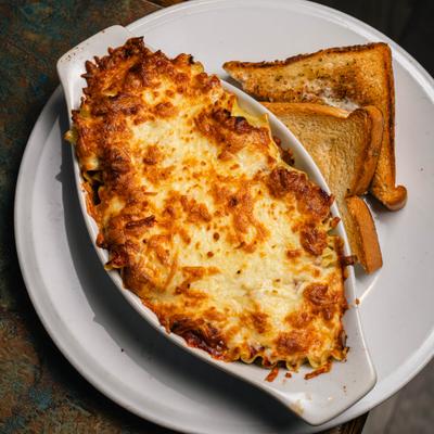 Baked lasagna served with toasted bread on white plate.