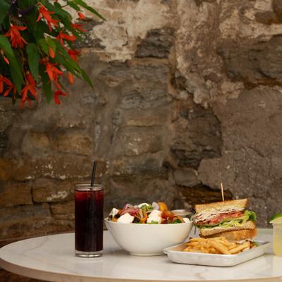 Sandwich with fries served alongside a bowl of salad and two cocktails.