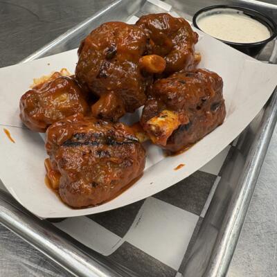 Saucy grilled pig wings served in a paper tray with a ranch dipping cup.