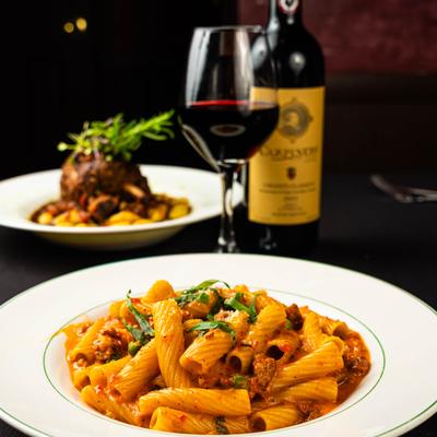 Rigatoni pasta with sausage and peas accompanied by red wine.