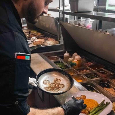 An employee arranging a dish with seared scallops on a plate at food bar.