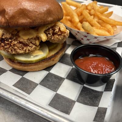 Crispy chicken sandwich with pickles and fries served alongside a small ketchup cup.
