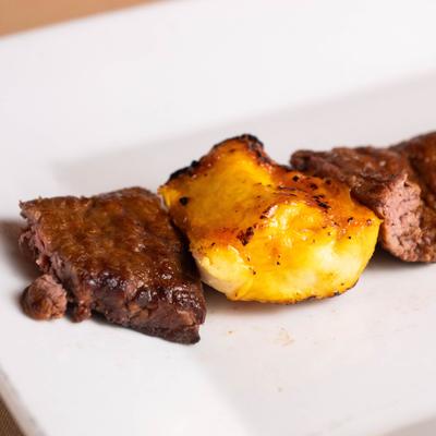 Grilled beef cubes beside a roasted potato wedge on a white plate.