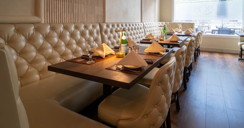 Restaurant interior with tufted leather seating, set tables, and large windows