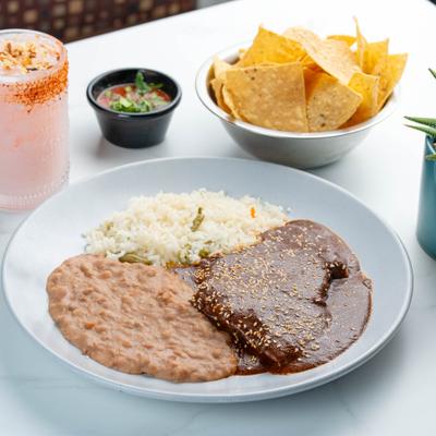 Chicken mole plate with beans and rice served with chips, salsa, and a cocktail.