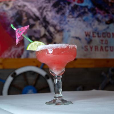 Strawberry margarita with a salted rim, lime, and paper umbrella garnish.