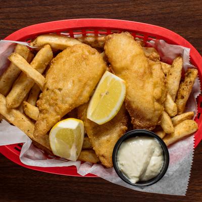 Basket of fish and chips with lemon wedges and tartar sauce.