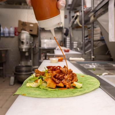 Chef pouring sauce on a burrito.