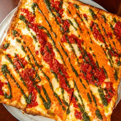 Square pizza with tomato sauce, vodka sauce, and pesto sauce drizzle.