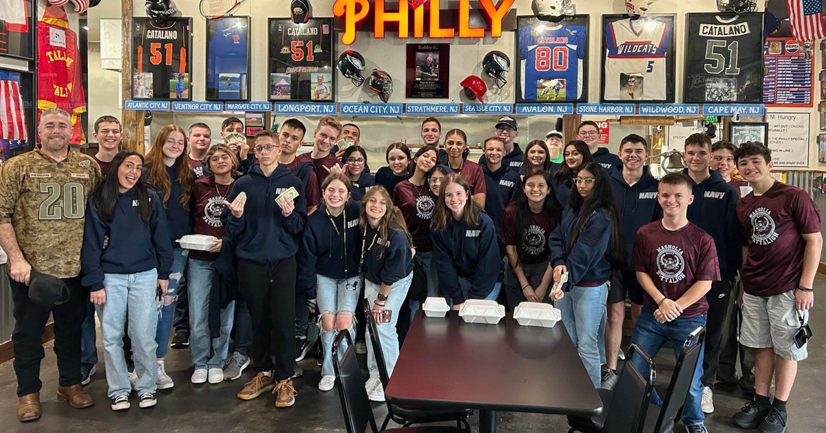A group of students in matching shirts posing in front of a wall with a Philly sign