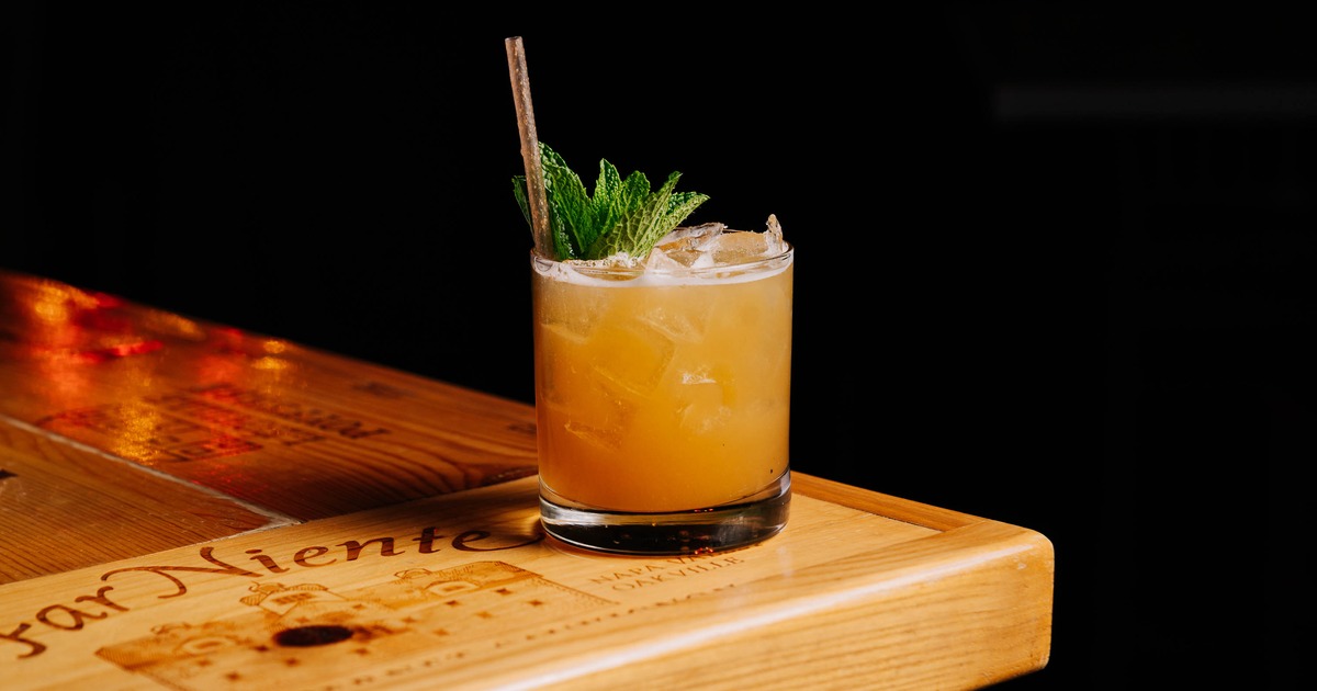 Peach Better Have My Bacon cocktail served on a wooden bar top