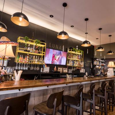 Bar area with wooden bar top, industrial-style lighting, and shelving with bottles.