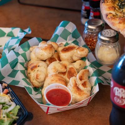 Garlic knots served in paper-lined basket with marinara sauce on the side.
