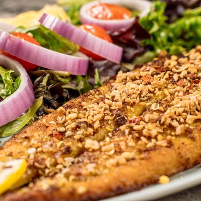 Tawa Machi fish served with greens, cherry tomatoes,  sliced red onion, lemon.