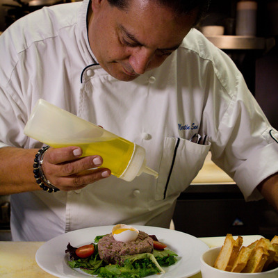 Chef drizzling dressing over a meat dish.