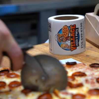 Employee slicing a pizza, and a roll of coated paper in the background.