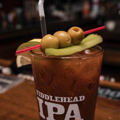 Bloody Mary garnished with three green olives, a celery stalk, and a lime wedge.