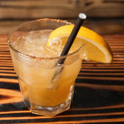 Iced cocktail with a salted rim and orange garnish served in a short glass.