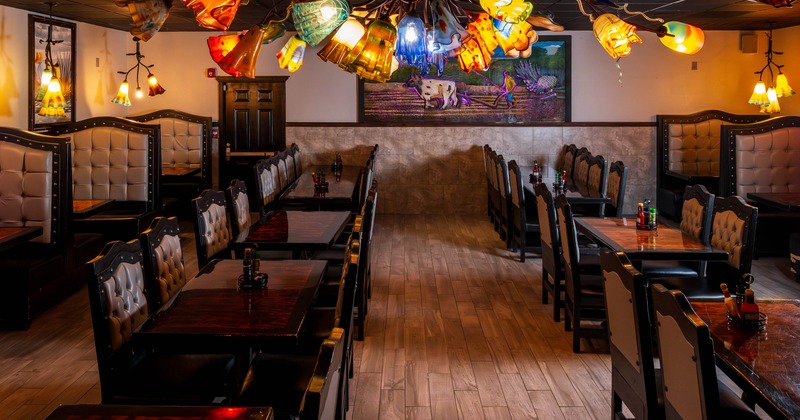 Interior of a restaurant with cushioned seating, colorful ceiling lights, and a rustic mural
