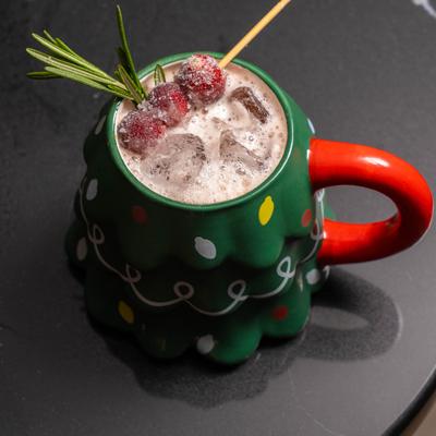 Cocktail with cranberry and rosemary garnish served in a ceramic mug shaped like a Christmas tree.
