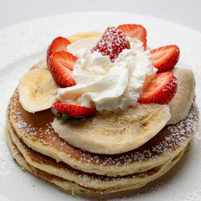Pancakes topped with banana and strawberry slices and whipped cream.