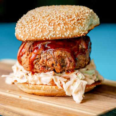 Pulled pork sandwich served on a sesame seed bun with a coleslaw and BBQ sauce.