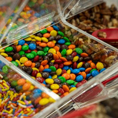 Clear plastic topping display featuring colorful chocolate candies and rainbow sprinkles.