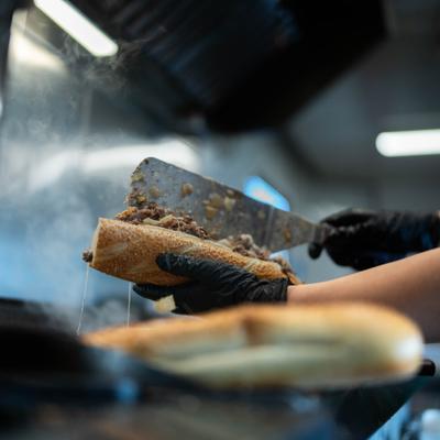 Chef preparing cheesesteak sandwich on a hot grill.