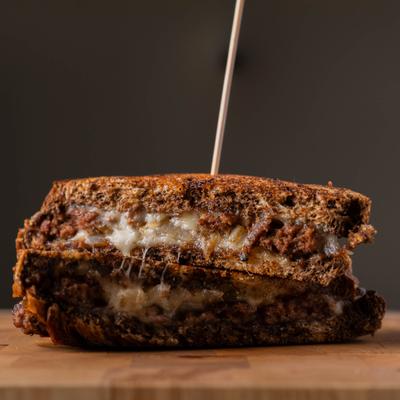 A thick toasted sandwich with melted cheese on a wooden cutting board.