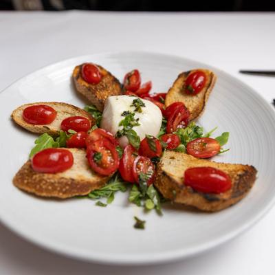 Crostini, with burrata cheese, grape tomatoes, and basil.