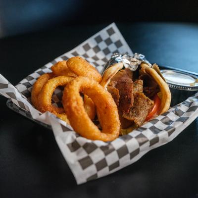 Lamb gyro sandwich served with onion rings and dipping sauce.