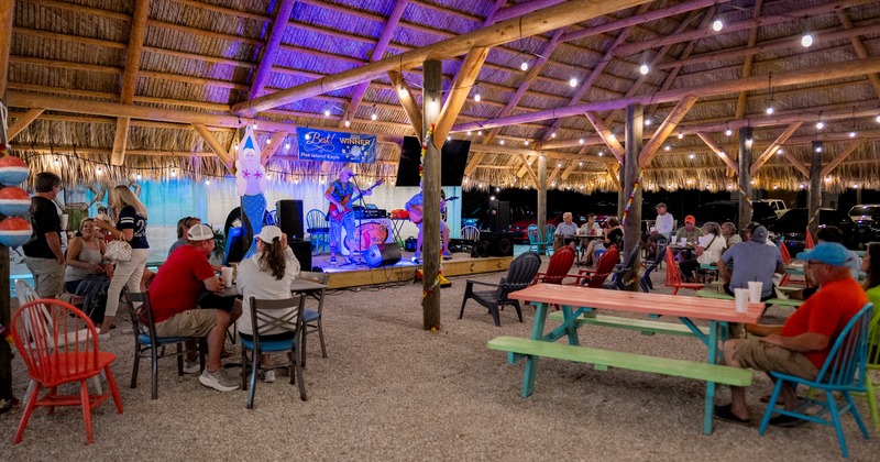 Covered outdoor seating area with guests enjoying their drinks, band playing music on a stage